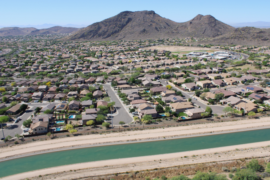 Aerial view of a large neighborhood in an arid mountain valley. Water flows by at the edge of the neighborhood, closest to the camera.