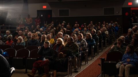 An audience in theater seats watching a screen