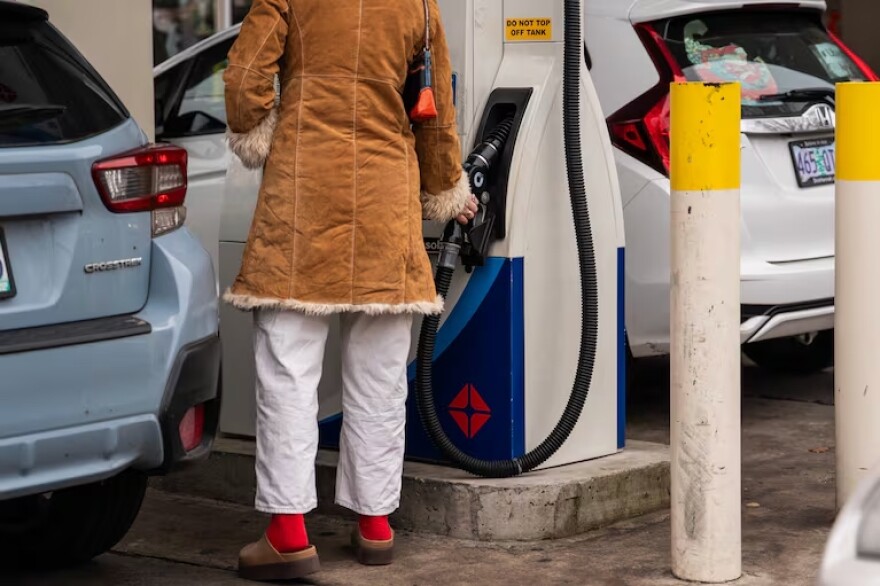 A person seen from behind stands next to their car at a gas pump
