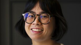 A woman wearing glasses and a white shirt smiles at the camera.