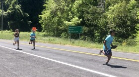 Axel Tripp from the Yurok Tribe carries a wooden salmon as he runs. He is followed by his sister Tahsa, a Yurok tribal member, and his cousin Julia Grant, from the Karuk tribe.