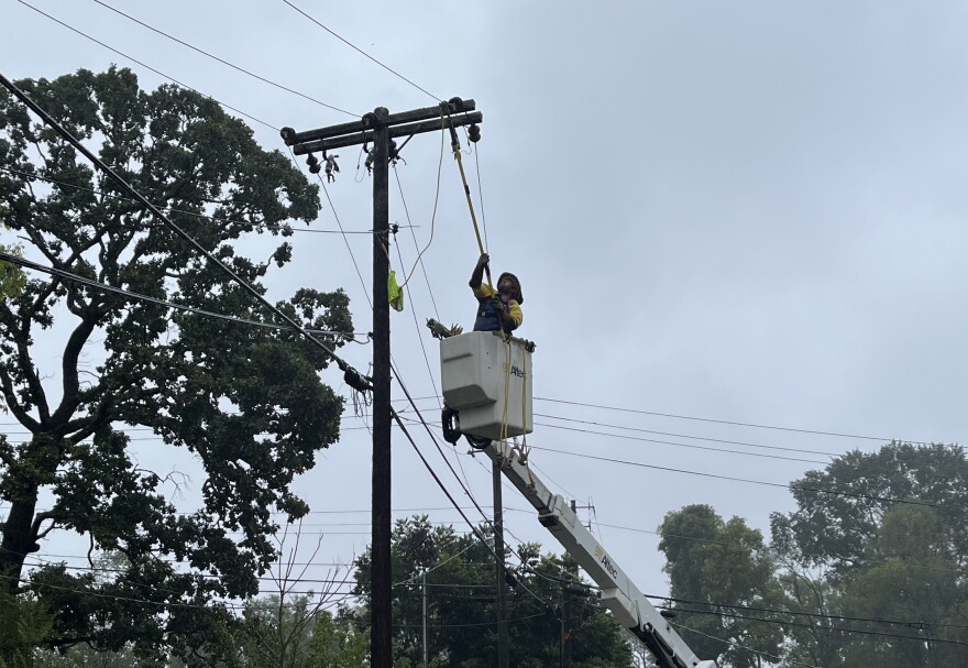 A lineman in the basket of a bucket truck reaches with a pole toward and electric line. 