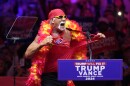 Hulk Hogan in yellow sunglasses, red bandana and red and yellow boa, ripping off his red T-shirt in front of a Trump Vance podium