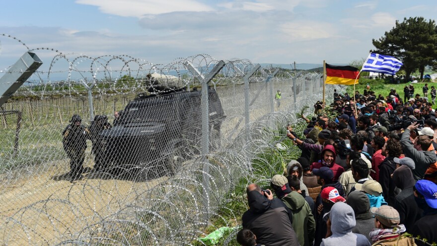 Refugees and migrants bearing Greek and German flags face Macedonian soldiers at the border fence as they protest on Monday, a day after violence broke out at the border.