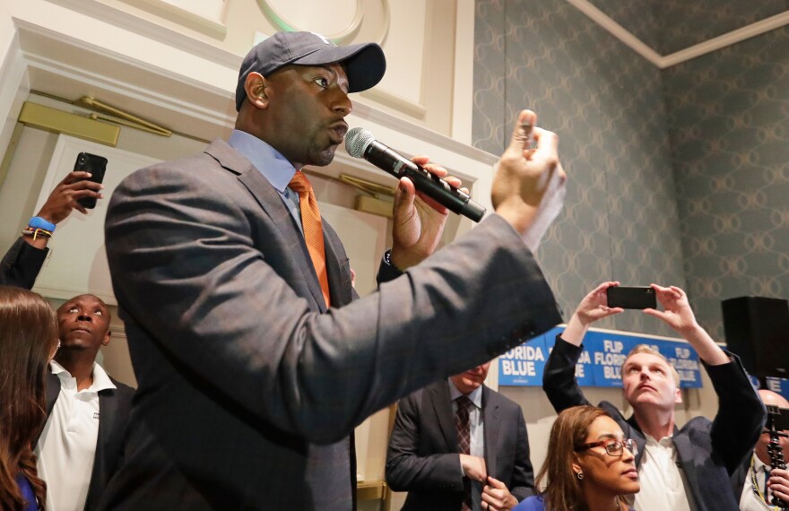 African American man in hat and suit talks into microphone with crowd 