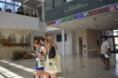 Young people with tote bags that read "USF" in green letters look down at their phones and walk across the lobby of a university building. 