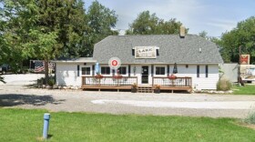 Bar and restaurant with white siding, a porch with limited seating and a slanted roof with a sign that reads 'Lake Road Inn'