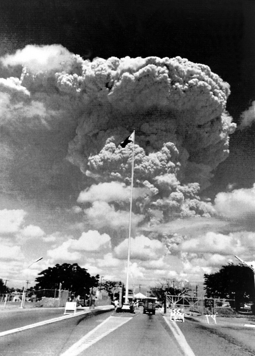 A Philippine flag flies over the gate to U.S.-run Clark Air Force Base in Angeles City, Philippines, June 12, 1991, as a cloud of volcanic ash from the erupting Mount Pinatubo looms in the distance.