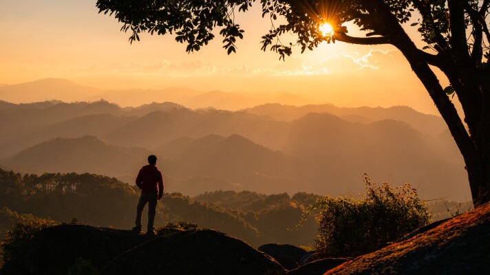 Successful young hiker man standing on top of mountain with the sun in the sunset at national park