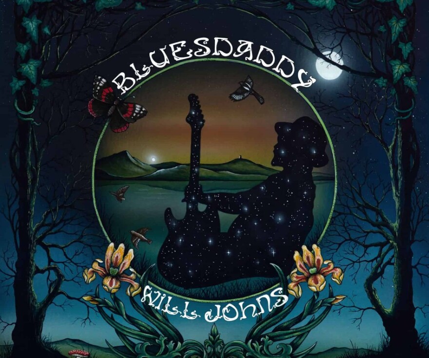 Album cover says BluesDaddy above a circle shape with a silhouette of a man playing a guitar with a bird flying and mountains in the background. Below the circle says Will Johns. The outside of the cover is a night sky with a moon at the top left and trees on either side 