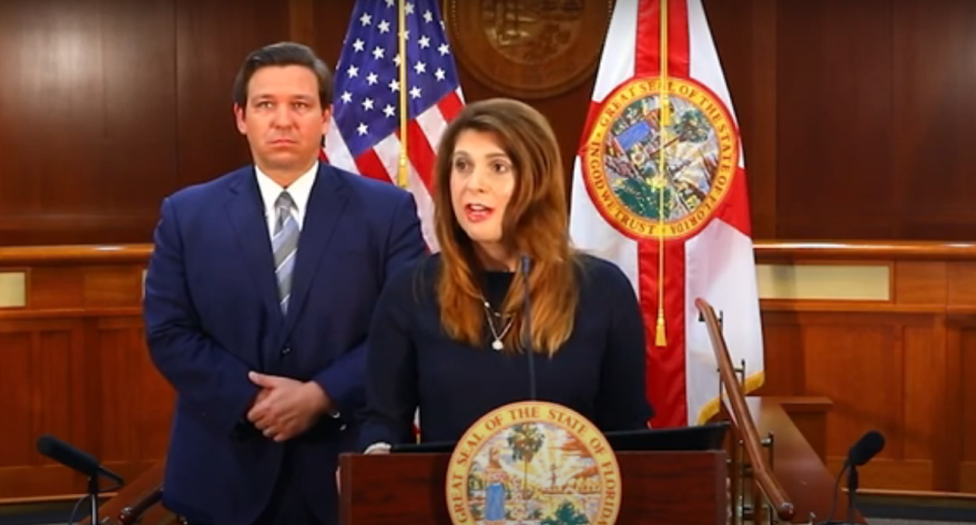 Woman at a podium speaking with a man standing behind her