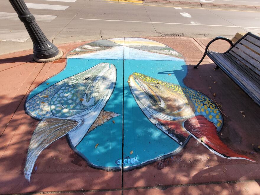 Painting of two fish in water; image is on a city sidewalk