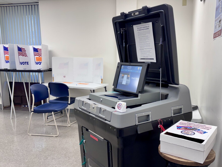 A gray voting machine sits open, with guarded places for voters to cast their ballots behind the machine.