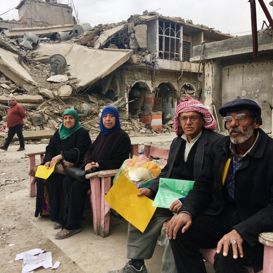 Samira Sheet (left) sits with neighborhood residents in Mosul's Old City, waiting for an aid organization they say has promised to give them money. They're holding folders with their IDs.