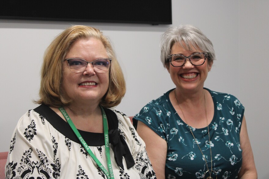 Two women sit next to each other smiling at the camera