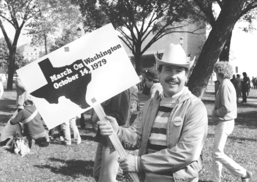 A black-and-white photo of Don Baker, a mustachioed man wearing a white cowboy hat. He's smiling and holding up a sign with a silhouette of Texas on it. The sign says "March on Washington, October 14, 1979."