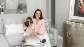 Mother posing with toddler daughter who is looking through a camera lens
