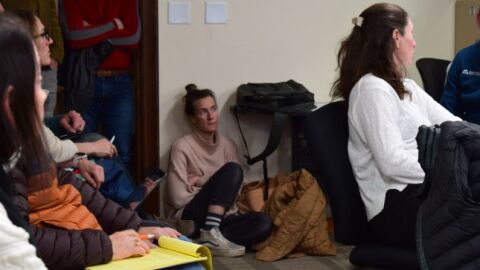 Steph Wise, Jackson Hole Community Housing Trust director of operations, sits on the floor near the door of the packed conference room in the basement of the “Old Teton County Library,” which is now office space.