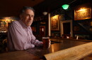 A man sits at a bar in a dimly-lit room with a pint.