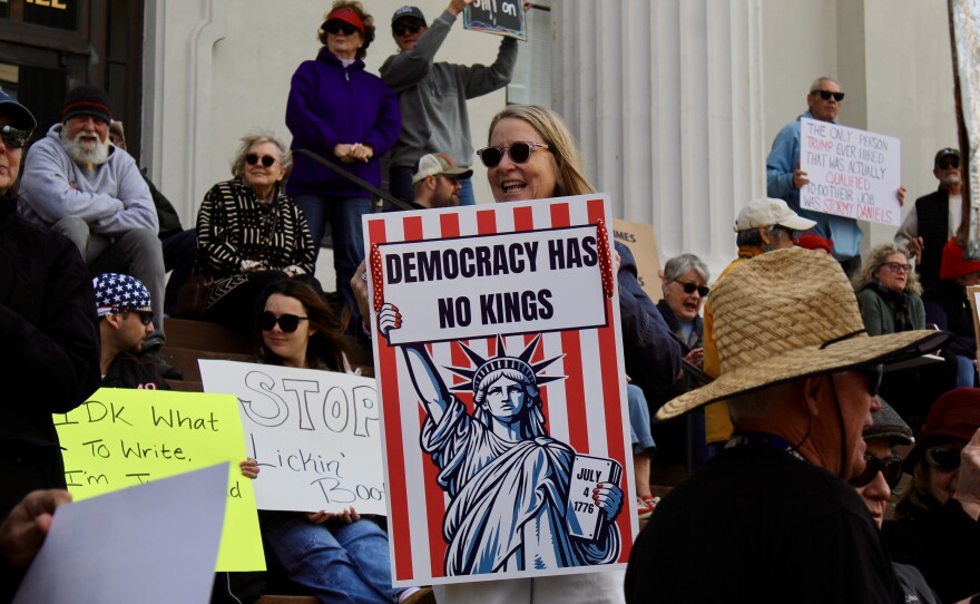 Protestors on the steps outside of Thalian Hall. Protestor (center) holding a sign stating "Democracy has no Kings."