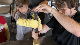 Glass artist, Anthony Remick, right, helps Jack, who was visiting the glass studio with his brother and parents, stamp into a piece of hot glass. This will become one of 1,000 glass medallions being hidden around Pierce County during the World Cup.