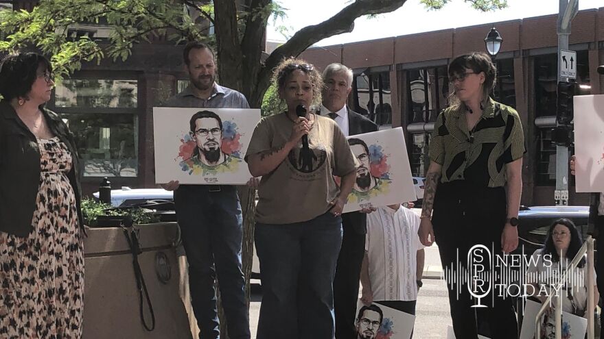 Rep. Natasha Hill (D-Spokane) speaks to gatherers after the guilty verdict handed to the "Spokane 3." She is flanked by illustrations of defendant Bajun Mavalwalla II, whose father is behind her, second from right.