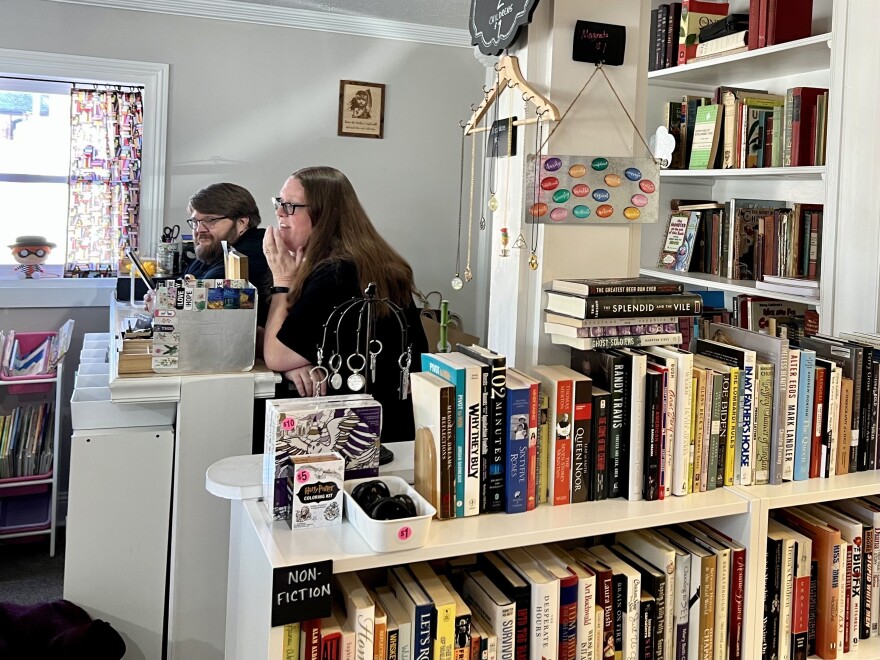 Rachel and Adam Collins sit behind shelves of nonfiction books. Knickknacks adorn the walls around them at their bookstore in Wilmington.