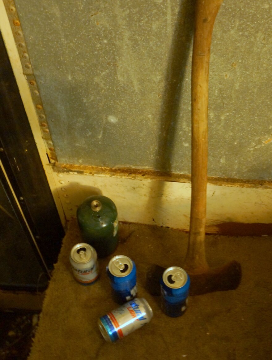An ax, some empty beer cans and a gas canister on the floor