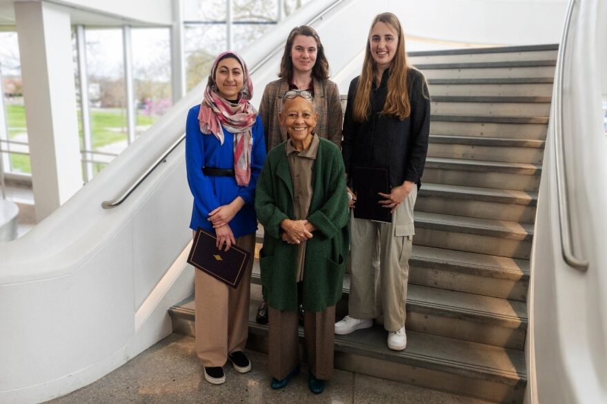 Nikki Giovanni poses in front of three undergraduate students who were awarded prizes in the 2024 Giovanni-Steger Poetry Ceremony. They stand on a staircase inside the Moss Arts Center. On the left is Ayah Ali, middle is Emily Paquette, and Caroline Foltz is in the right.