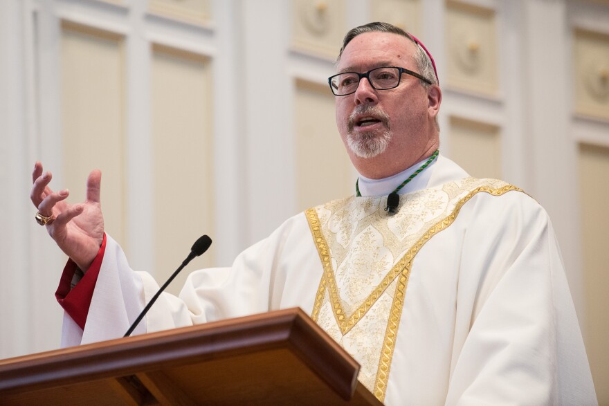 A man in a white robe stands at a podium to speak
