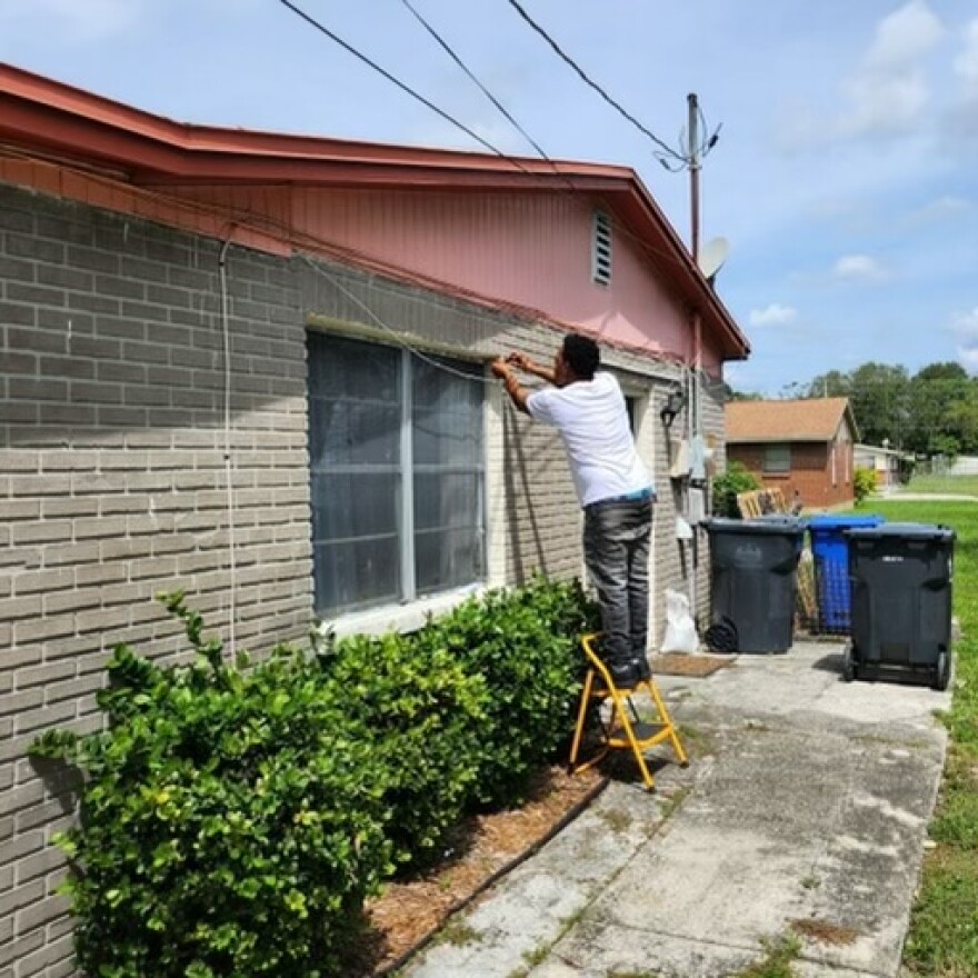 Man standing on a yellow step ladder adjusting windows from the outside of a home. 