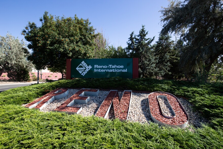 A sign outside that says, “Reno Tahoe International Airport,” with a sign beneath it in the grass that says, “RENO,” in large letters.