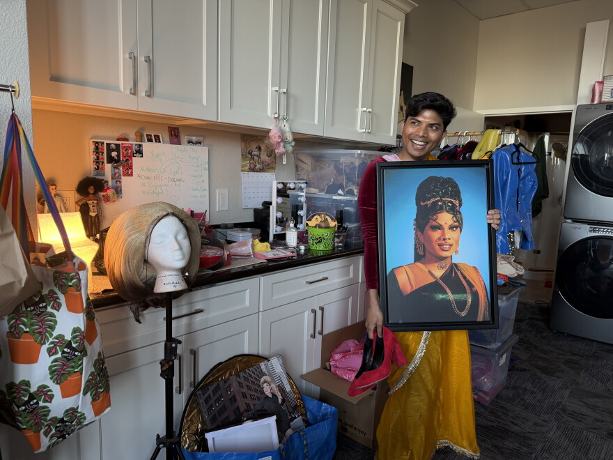 Raj Krishna, holding a portrait of his drag persona, Bindi Masala, in his Oakland apartment, May 2026.