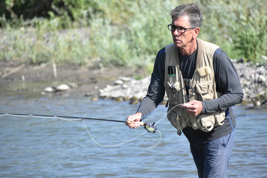 A man holds a fly fishing pole in front of a river.