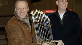 FILE - Boston Red Sox CEO Larry Lucchino, left, and Chief Operating Officer Sam Kennedy hold the 2013 World Series baseball trophy on the red carpet at the Wang Theatre before a screening of a DVD about the series in Boston, Nov. 23, 2013.