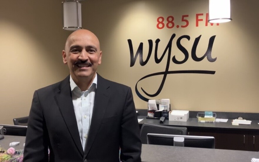 Juan Santiago facing the camera smiling with the words "88.5 FM WYSU" behind him on the wall