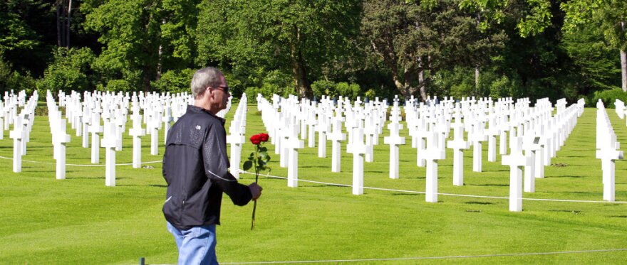 A visitor carrying a red rose walks among graves at the Colleville American military cemetery, in Colleville sur Mer, western France, Saturday June 6, 2015, on the 71th anniversary of the D-Day landing. D-Day marked the start of a Europe invasion, as many thousands of Allied troops began landing on the beaches of Normandy in northern France in 1944 at the start of a major offensive against the Nazi German forces, an offensive which cost the lives of many thousands.(AP Photo/Remy de la Mauviniere)