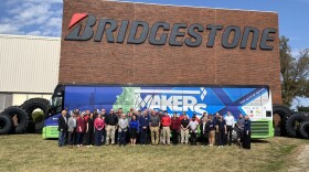 A large group of people standing in front of the "Makers on the Move" bus while it is parked in front of the Bridgestone Americas building in Normal.