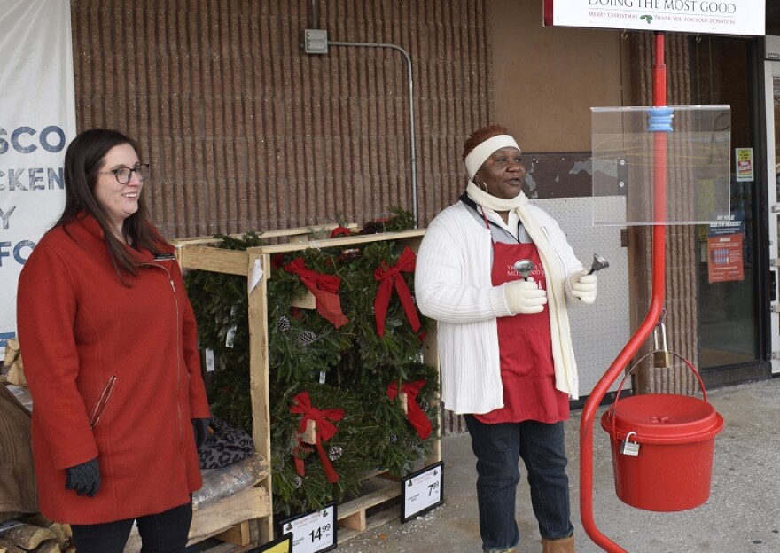 Two women stand near a red kettle. 