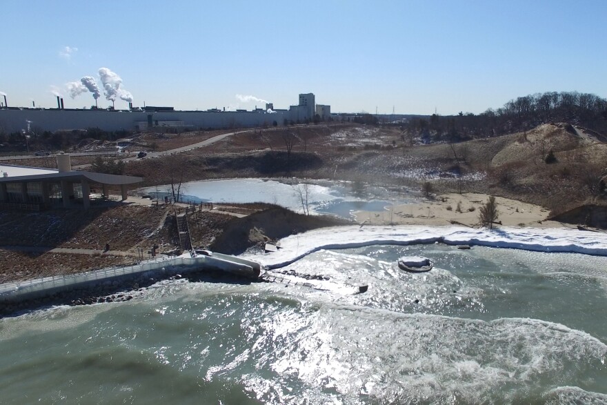 The sunken pier is surrounded by dunes and a national park building, with industrial facilities in the background. 