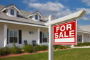 A white apartment buildings with a red sign in front of it that says "For Sale". 