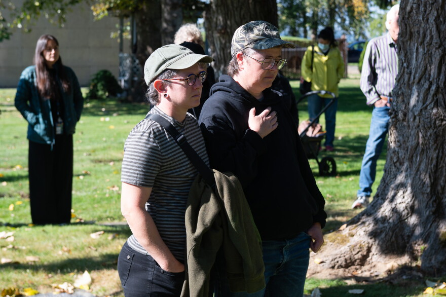 People stand in a sunny field near a tree. 