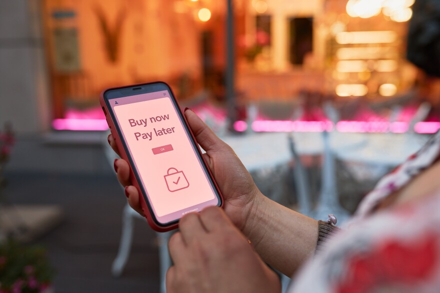 A woman holds up a phone screen with a 'Buy Now, Pay Later' advertisement up. 