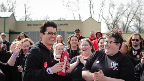 People wearing black t-shirts and hoodies smile while one person holds a red envelope