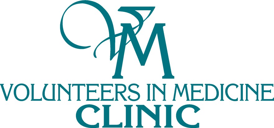 Teal logo for Volunteers in Medicine Clinic, featuring a stylized script "VM" monogram above the organization's name in serif type, with "Clinic" in bold letters below.