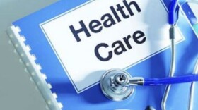  A stethoscope lays on top of a blue notebook that reads "Health Care."