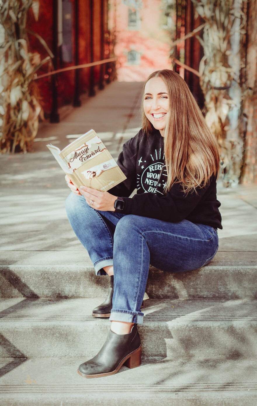 Author Cecilia Garcia, seated on steps holding her book
