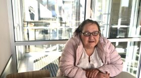  A photo of Susan Bell in a pink puffer jacket, resting her arms on a table.