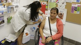 In this Oct. 1, 2013, file photo, Walgreens' pharmacist, Jennifer de Jesus, left, administers a free influenza vaccine to Ana Navarro, 33, during the Binational Health Week event held at the Mexican Consulate in Los Angeles. The flu has hit California so hard this year, pharmacies have run out of medicine to treat it, emergency rooms are packed and the death toll is rising. The Los Angeles Times reports that 27 people younger than 65 have died of the influenza in California since October. (Damian Dovarganes/AP)