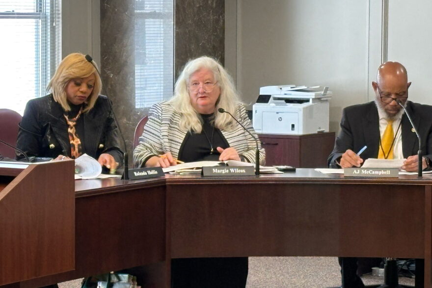 Alabama Representative Margie Wilcox is flanked by two other state representatives. They sit behind a desk.